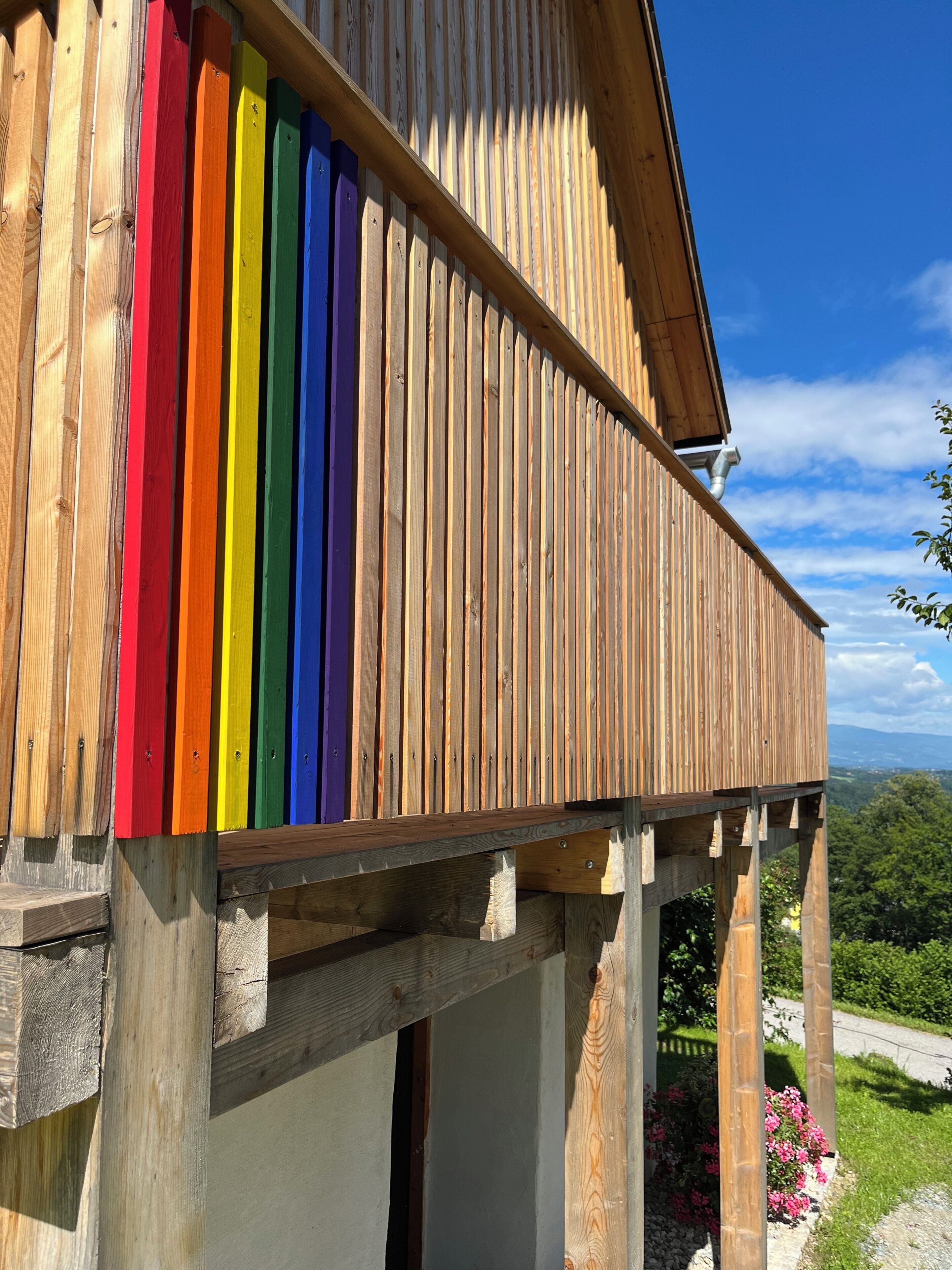A wooden building with a balcony featuring a rainbow-colored railing.