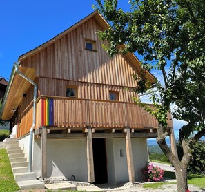 Ein Holzhaus mit Balkon, einer Treppe zum Eingang und Blick auf die umliegende Landschaft.