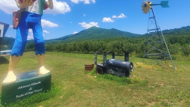 Eine Statue, die einen Charakter zeigt, der einen Apfel hält, mit einer Windmühle im Hintergrund und einem Schild für Johnson's Orchards & Peaks of Otter Winey.