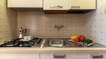 Una cocina con estufa a gas, un lavamanos y un frutero con diversas frutas.