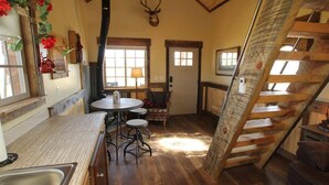 Ein rustikales Interieur mit einer Holztreppe, einem Essbereich mit rundem Tisch und Hockern sowie einer Küche mit Spüle.