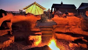 Ein Campingplatz mit Zelt, einem kleinen Gebäude und einem Lagerfeuer.