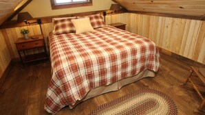 Ein Schlafzimmer mit schrägen Wänden, einem Bett mit karierter Bettdecke, einem Nachttisch mit Lampe und einem kleinen Fenster.
