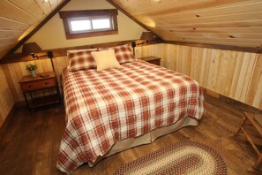 A bedroom with a sloped ceiling, a bed with a plaid bedspread, a nightstand with a lamp, and a small window. - Little Rock Cabin Near Zion and Bryce Canyon Views (Cane Beds)