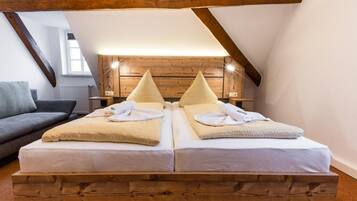A room with two beds, a wooden headboard, a gray sofa, and a sloped ceiling.