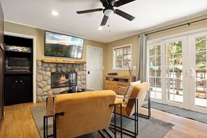 A living room with a fireplace, a ceiling fan, a television, and a view through glass doors. - Lovely Studio cabin in peaceful Green Valley Lake. (Green Valley Lake)