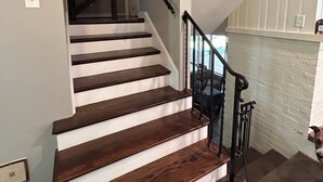 Eine Treppe mit Holzstufen und einem schwarzen Geländer, die zu einer Zwischenebene mit einer weißen Wand und einem Kamin führt.