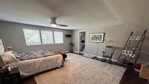 Ein Schlafzimmer mit Bett, Teppich, Deckenventilator, Fenster und einer Tür zu einem Badezimmer.