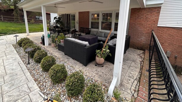 Eine überdachte Terrasse mit Gartenmöbeln, einer Ziegelwand und einem weißen Geländer.