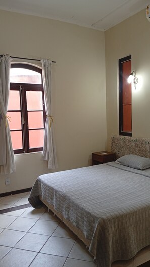 A bedroom with a bed, a nightstand, a window with curtains, a wall-mounted light, and a patterned headboard. - Direita S.Antonio -Comfort quarter and hall, view centro historico. (Salvador)