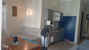 A compact living space with a sofa, a dining table, a kitchenette, and a standing fan. - Direita S.Antonio -Comfort quarter and hall, view centro historico. (Salvador)