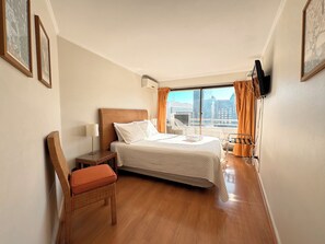 Ein Hotelzimmer mit Bett, Sessel, Nachttisch, Fernseher und einem Fenster mit Vorhängen.
