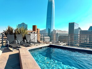 Une piscine sur le toit, avec des chaises longues et une vue panoramique sur la ville en arrière-plan.