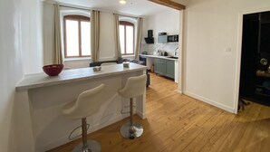 A modern kitchen with a wooden ceiling, a white countertop, two bar stools, and a window with curtains. - Movies and board games, quiet accommodation (Arlanc)