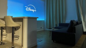 A living room with a flat-screen TV displaying the Disney+ logo, a sofa, a coffee table, and a bar stool. - Movies and board games, quiet accommodation (Arlanc)