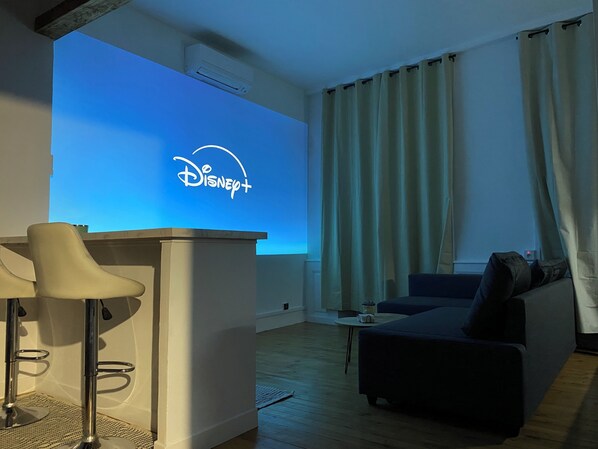 Un salon avec un téléviseur à écran plat affichant le logo de Disney+, un canapé, une table basse et un tabouret de bar.
