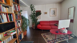 Olohuone, jossa on punainen sohva, puinen kirjahylly, pöytätietokone ja kuviollinen matto.