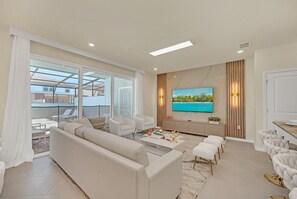 Ein modernes Wohnzimmer mit Sofa, Couchtisch und Fernseher. Ein Balkon bietet Blick auf das Meer.