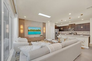 Ein modernes Wohnzimmer mit großem Flachbildfernseher, einer Couch und einer Küchenzeile mit Barhocker.