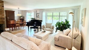 A spacious living room with a piano, sofas, a dining area, and large windows. - Clean and Convenient 4-bedroom house in Pittsford! (Pittsford)