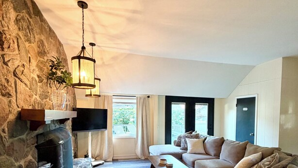 A living room with a stone fireplace, a sofa, a coffee table, and a view of the outdoors. - Clean and Convenient 4-bedroom house in Pittsford! (Pittsford)