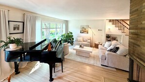 A living room with a grand piano, a sofa, a coffee table, and a staircase. - Clean and Convenient 4-bedroom house in Pittsford! (Pittsford)