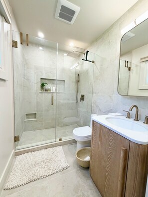 Une salle de bain moderne avec une douche à parois de verre, un lavabo blanc avec un meuble-vasque en bois et un grand miroir.
