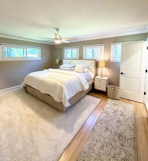 Une chambre à coucher comprenant un lit, des tables de chevet, une lampe, un ventilateur de plafond et une porte.