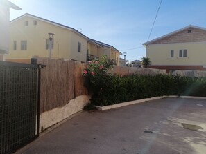 Eine Wohnstraße mit Häusern, einem verschlossenen Eingangstor und blauem Himmel.