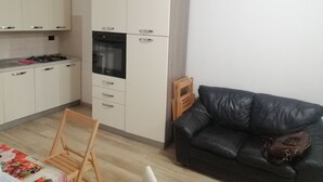 Moderni keittiö, jossa on valkoiset kaapit, musta uuni ja ruokailutila, jossa on puinen tuoli ja pöytä.