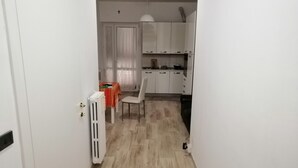 Kapea käytävä johtaa ruokailutilaan, jossa on pöytä ja tuoleja. Taustalla näkyy patteri ja valkoiset kaapit.