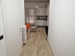 Ein schmaler Flur, der zu einem Essbereich mit Tisch und Stühlen führt. Im Hintergrund sind eine Heizung und weiße Schränke zu sehen.