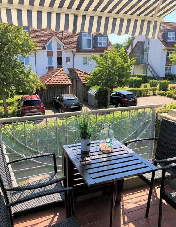 A balcony with a table, chairs, a potted plant, and a glass container. - Large Baltic Sea Nest (Boltenhagen)