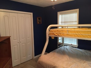 A bedroom with a bunk bed, a wardrobe, and a window with blinds.