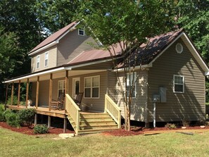 A two-story house with a porch, a staircase, and a small tree in front.