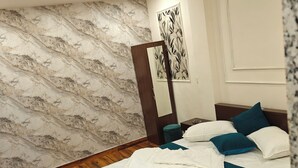 Une chambre avec un plancher en bois, un lit avec une literie blanche et turquoise, un miroir et un mur à motifs de marbre.