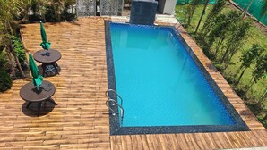 Une piscine rectangulaire entourée d’une terrasse en bois, avec une échelle en métal et deux parasols verts.