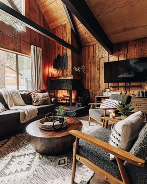 A cozy cabin interior with a fireplace, wooden walls, a sofa, a chair, and a television. - Firefly Cabin with Mountain View (Big Bear Lake)