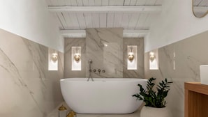 A modern bathroom with a freestanding bathtub, marble walls, and wall-mounted sconces. - Carla, elegant and romantic studio suite on the 2nd floor in the city of Noto (NOTO)