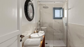 Un baño moderno con ducha acristalada, un espejo redondo y un mueble de tocador con lavabo y toalla.