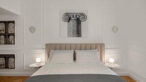 Un dormitorio con una cama grande, dos mesitas de noche con lámparas, una obra de arte con motivos de columna y cuadros enmarcados en las paredes.