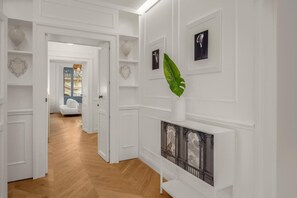 Een gang met witte wanden, een houten vloer en een witte deur die naar een andere kamer leidt.