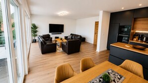Una sala de estar moderna con televisor de pantalla plana, sofás de cuero, una mesa de comedor de madera y una zona de cocina con armarios oscuros y encimera de madera.