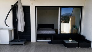 Ein modernes Schlafzimmer mit Bett, einer kleinen Sitzecke und einer Schiebetür zum Balkon.