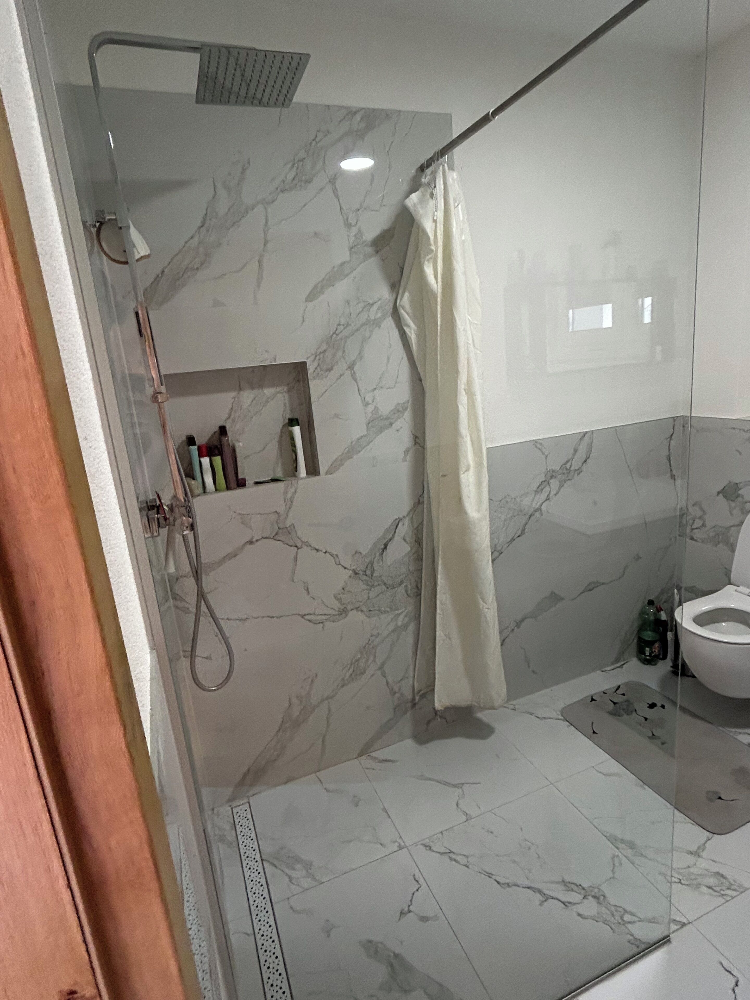 Un baño con ducha, inodoro y azulejos de mármol.