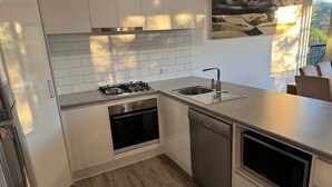 Una cocina moderna con muebles blancos, un lavamanos de acero inoxidable, horno empotrado y lavavajillas.