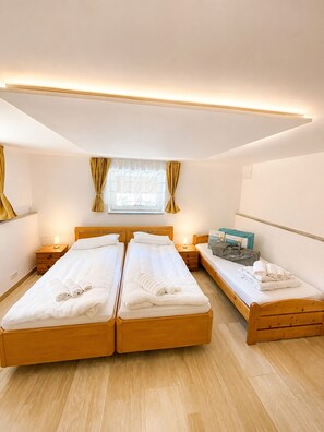 A hotel room with two wooden beds, a small desk, a window with curtains, and a wall-mounted air conditioning unit. - Villa on Lake Wangermeer—North Sea Vacation, Terrace, Dog-Friendly, Up to 5 Guests (Wangerland)