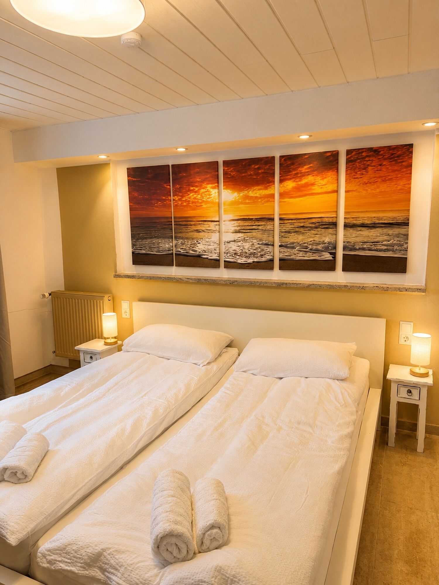 Ein Hotelzimmer mit zwei Betten, einem großen Sonnenuntergangsgemälde über den Betten und Nachttischlampen.