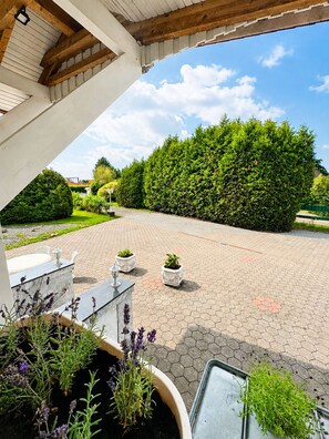 A covered outdoor area with a paved walkway, potted plants, and a view of a well-maintained hedge and garden. - Villa on Lake Wangermeer—North Sea Vacation, Terrace, Dog-Friendly, Up to 5 Guests (Wangerland)