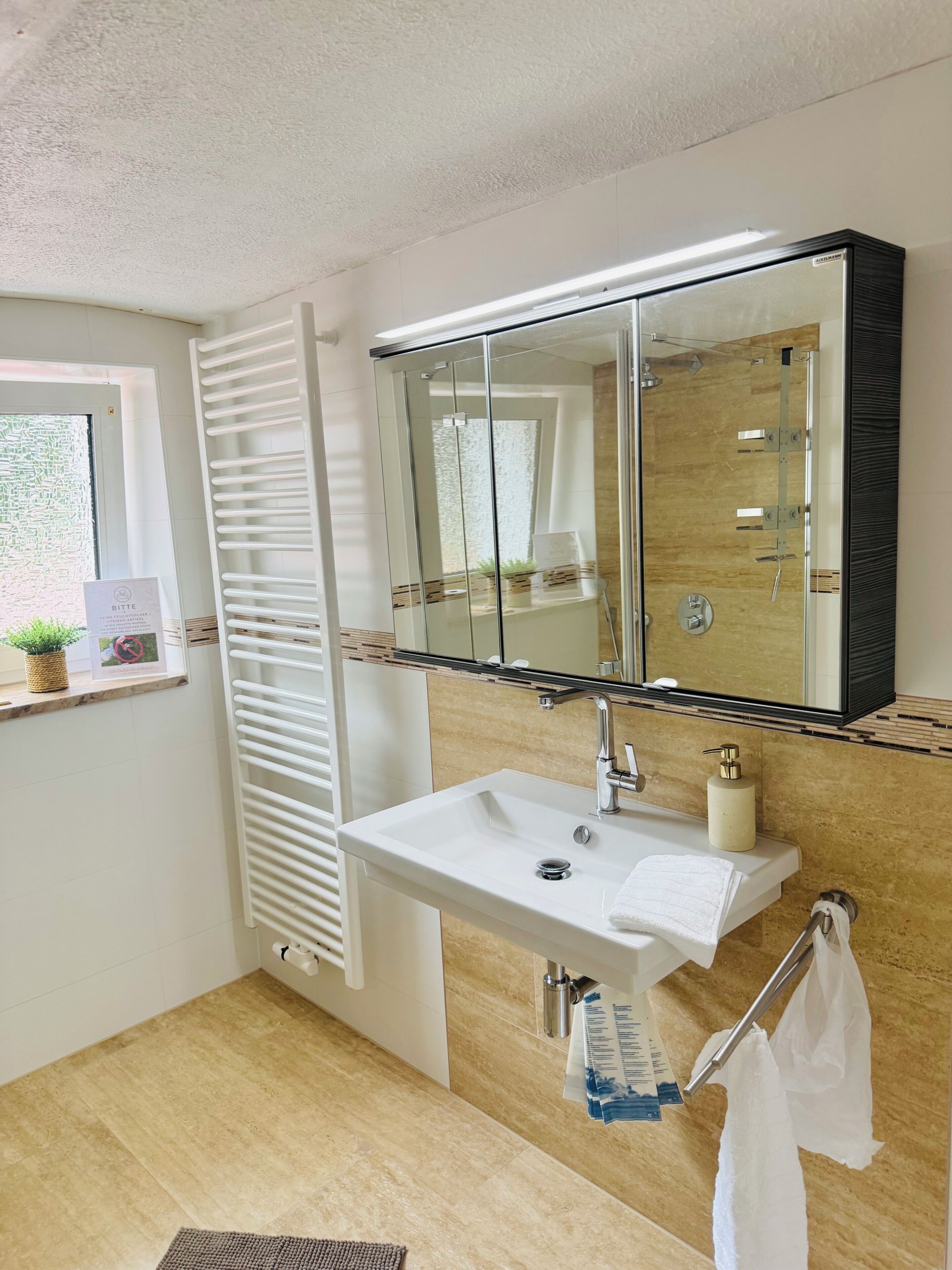 Un bagno moderno con cabina doccia in vetro, un lavandino bianco con specchio sopra e un porta asciugamani.
